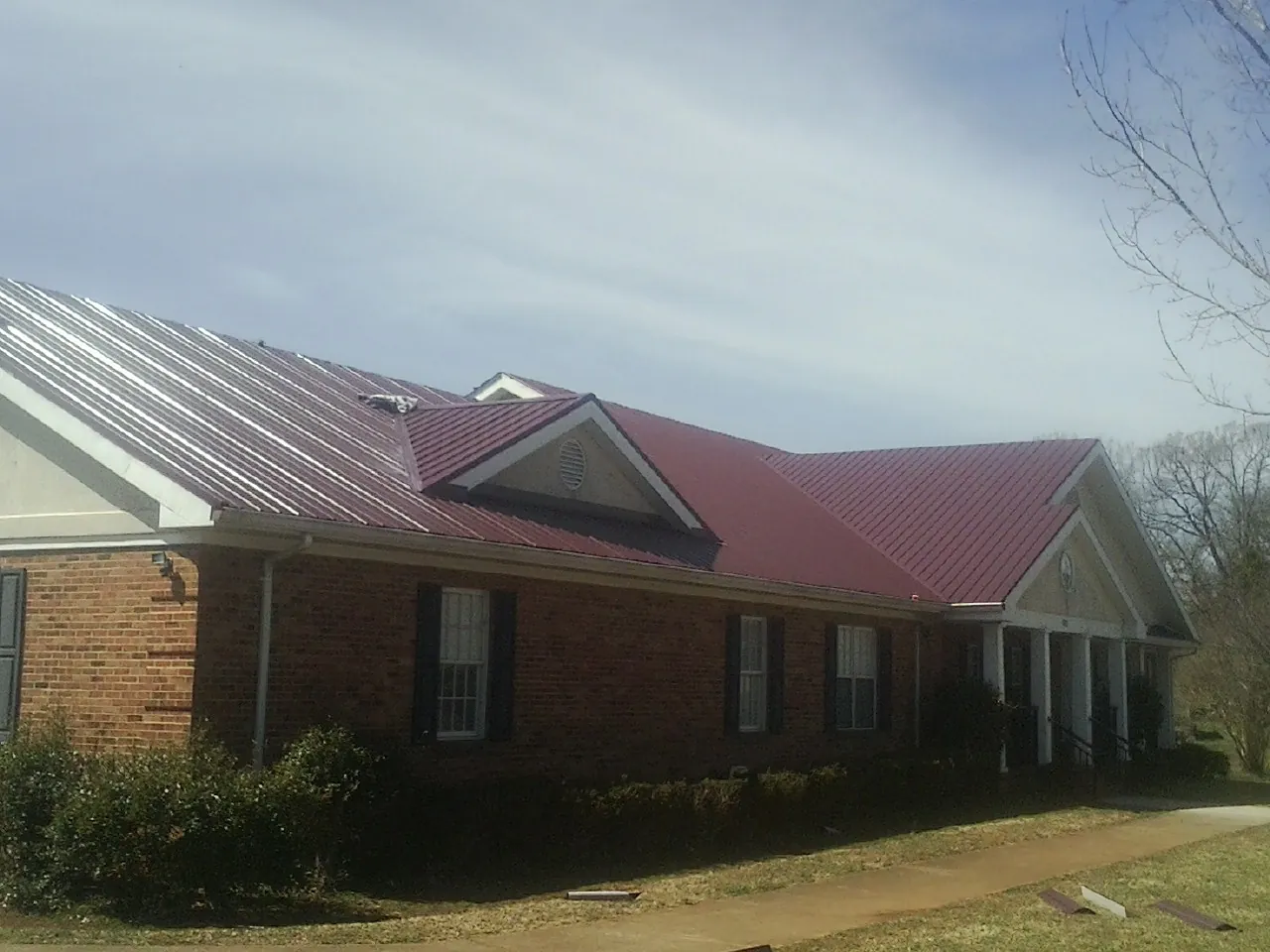 Red metal roof with gabled entries on a long brick building, from a Hail Damage Roof Repair job in Kingston